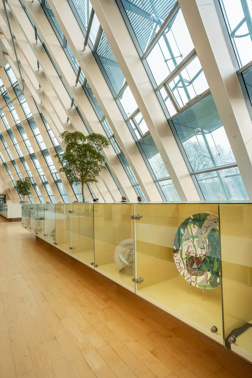 In de bibliotheek aan het Smallepad te Amersfoort, zicht op vitrines met kunst en daarachter raampartijen van het gebouw