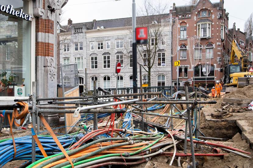Openliggende straat in de grachtengordel in Amsterdam, met op de voorgrond kabels in verschillende kleuren en op de achtergrond werkers en een graafmachine.