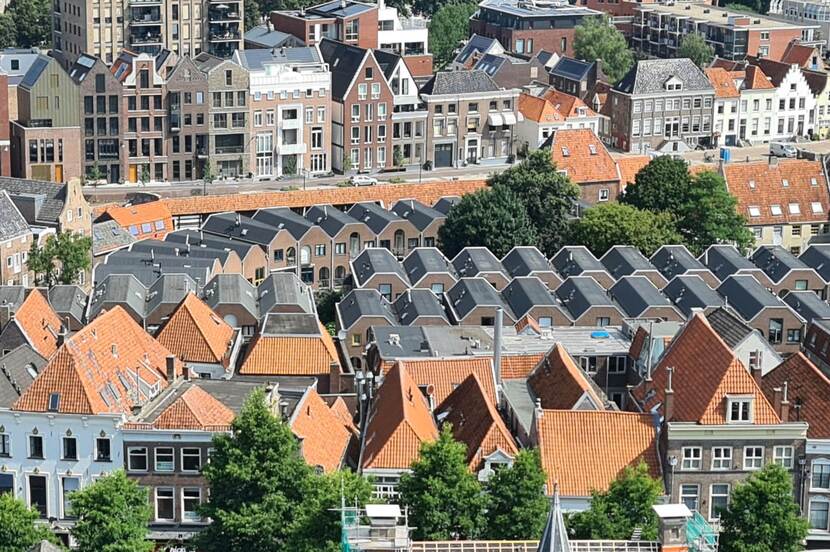 Foto van boven van dicht op elkaar gebouwde huizen in verschillende stijlen: van klassiek ogende panden met oranje daken tot nieuwere bebouwing met grijze daken.