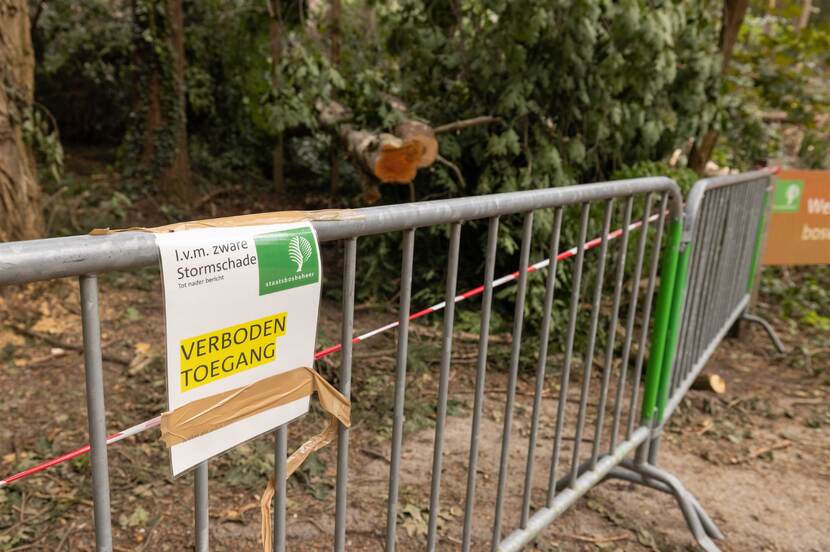 Ijzeren hek op een bospad met daarop geplakt een bordje met de tekst 'Verboden toegang i.v.m. zware stormschade'.