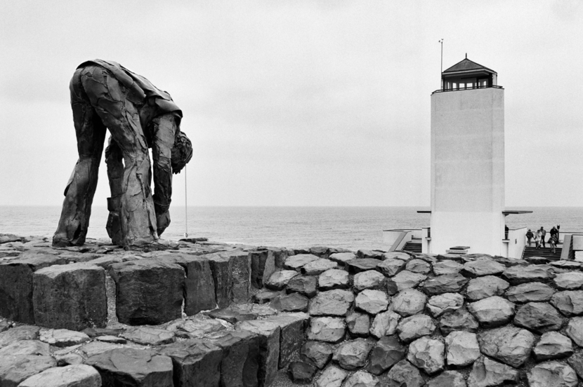 Beeld De steenzetter met op de achtergrond het Vlietermonument