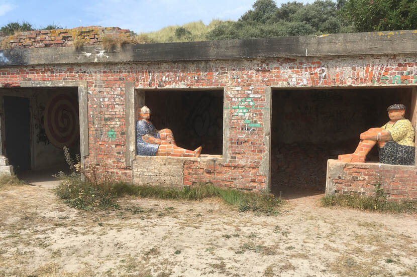 Foto van een gemetselde bunker op Terschelling in de duinen met daarin twee beelden van een man en een vouw