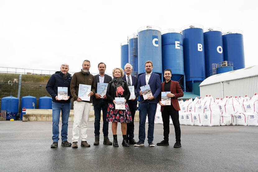 Foto van een rij van zeven personen die een publicatie ophouden: de visie op de Atlantikwall en de Atlantikwall Atlas, voor een aantal blauwe silo's met de letters CEBO.