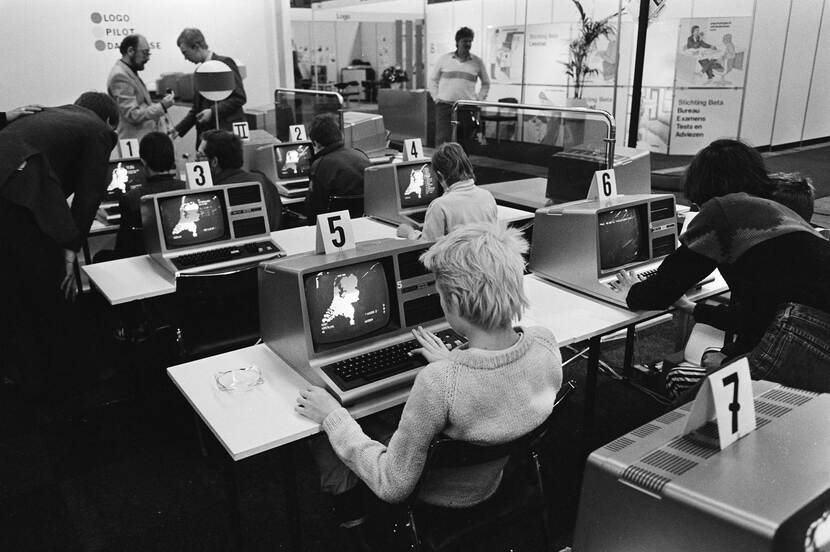 Zwart-wit foto van een klas vol leerlingen die op de computer werken met een paar leraren vooraan de klas.