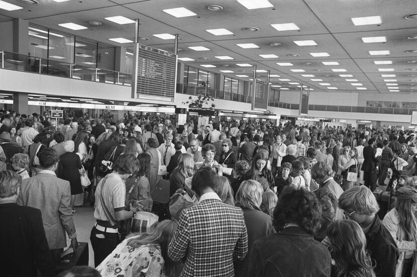 Zwart-wit foto van een grote groep mensen die wachten in Schiphol.