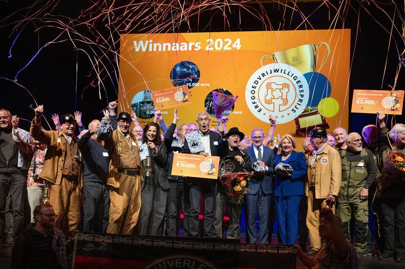 Foto van een groep uitgelaten mensen op een podium met een cheque van 10.000 euro bij de uitreiking van de erfgoedvrijwilligersprijs 2024